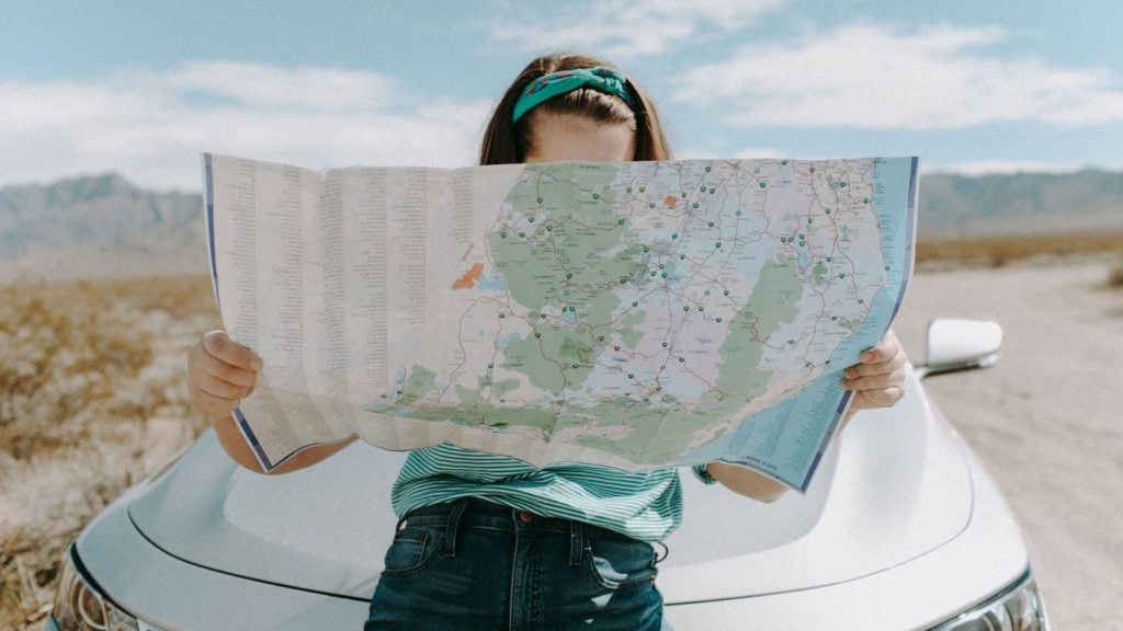 Woman leaning against car holding map (Photo: Leah Kelley via Pexels)