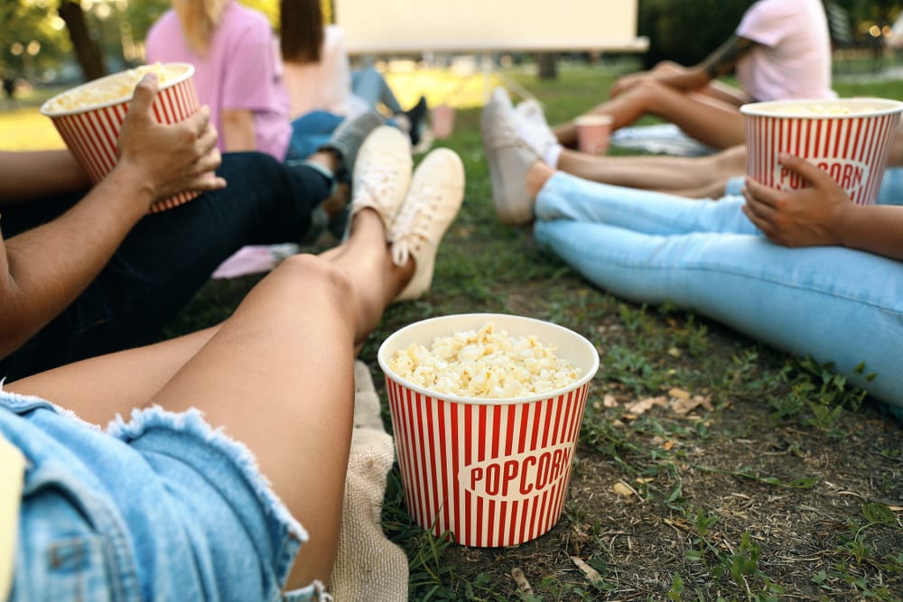 Outdoor movie screens: Young people with popcorn watching movie in open air cinema. (Photo: Shutterstock)