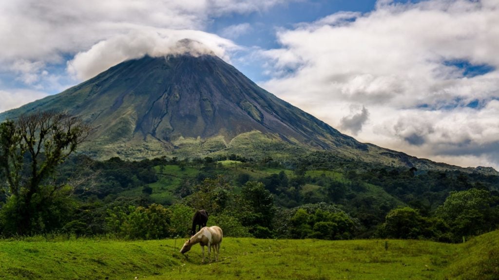 Arenal Volcano di Kosta Rika dikelilingi oleh awan dengan kuda merumput di latar depan