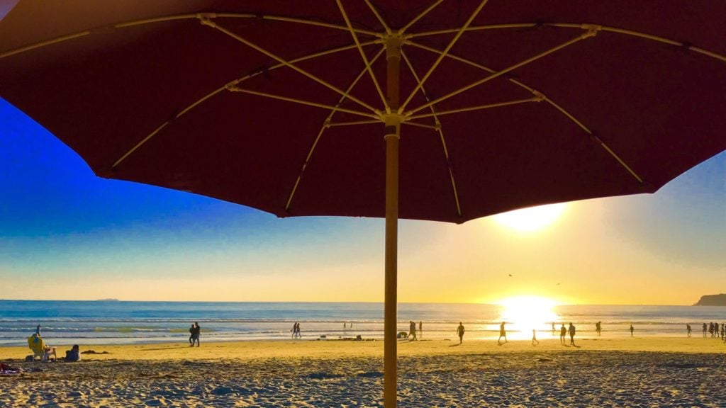 View of beach and water at sunset from under a beach umbrella in Coronado, California, a skip-gen vacation destination