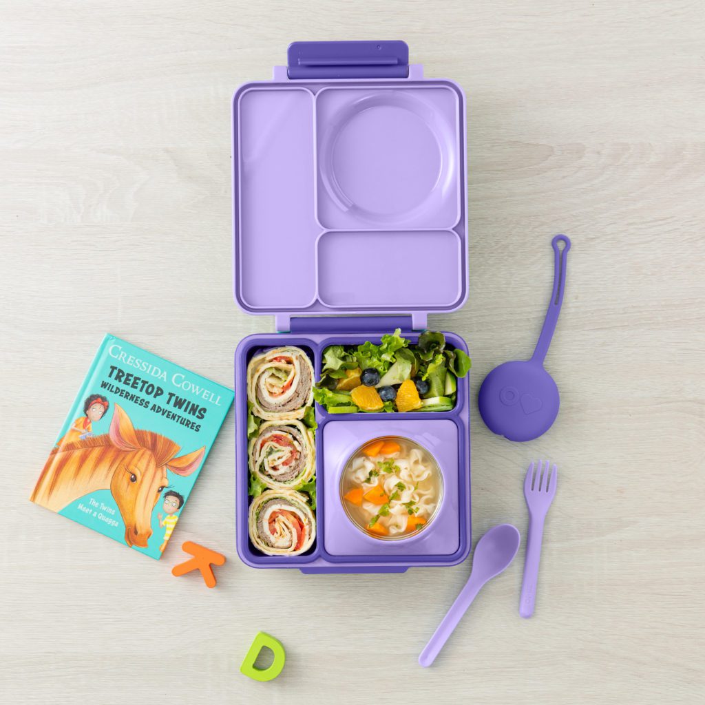 Purple OmieBox Bento Box with lunch items, utensils, and a book
