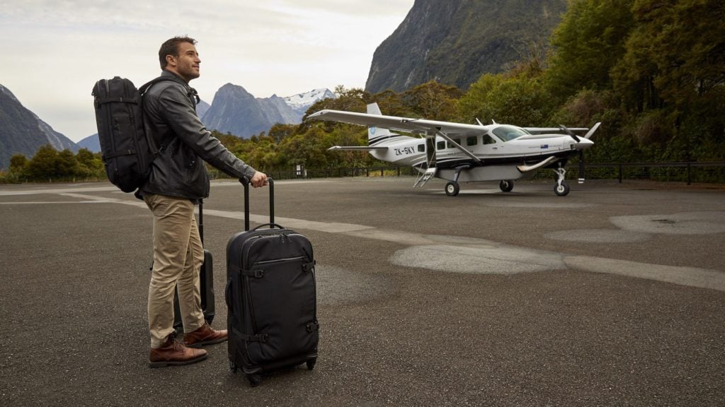Man on a small runway with Eagle Creek luggage and a small plane in the background