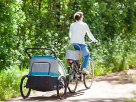 Young mother riding bicycle with baby bike trailer in sunny summer park. (Photo: Shutterstock)