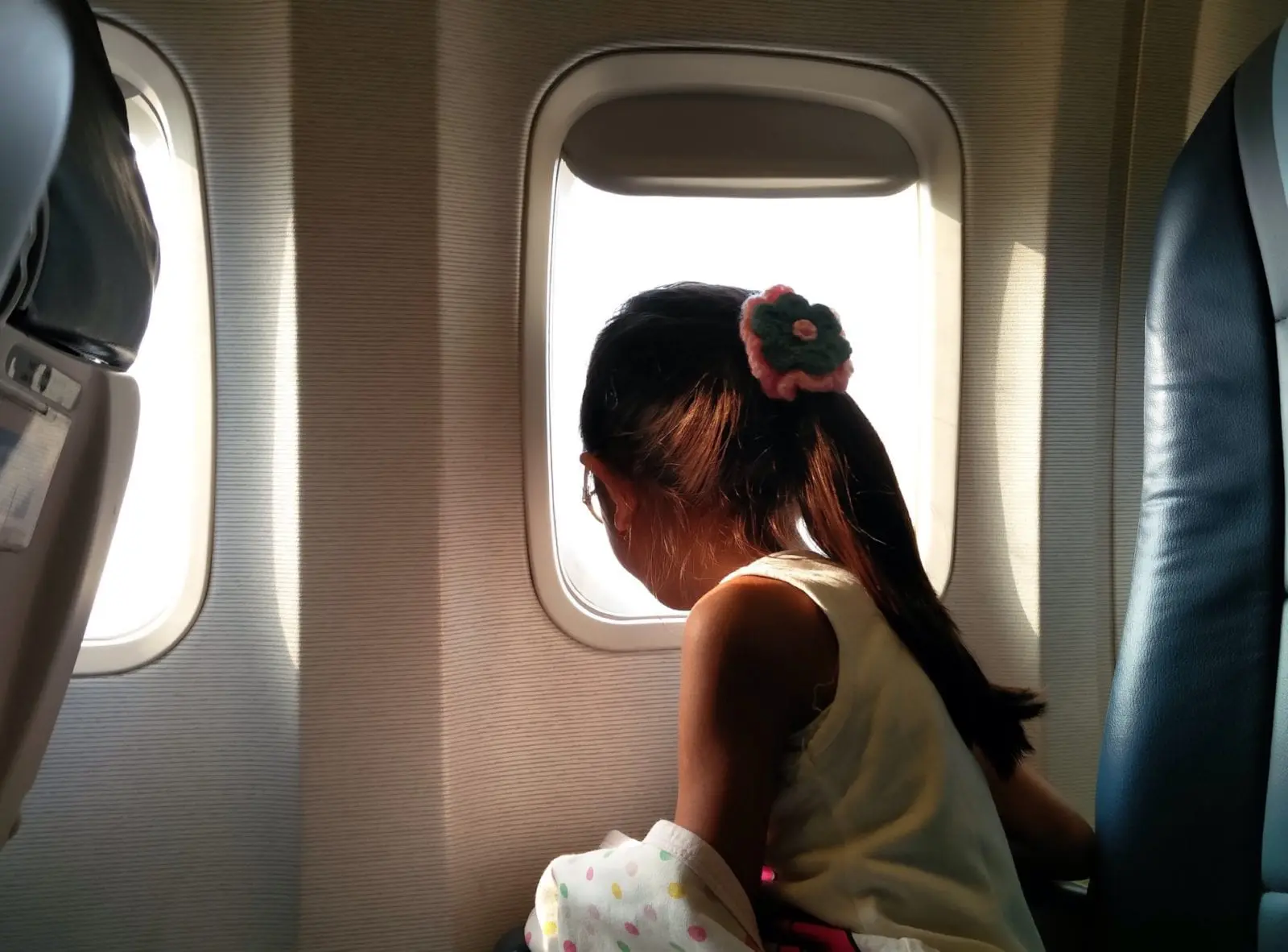 child with ponytail looking out airplane window