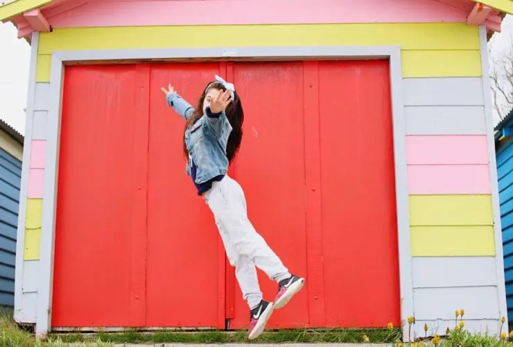 girl in sneakers jumping in front of colorful house