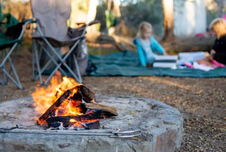 camp fire with kids playing on a blanket 10 feet away