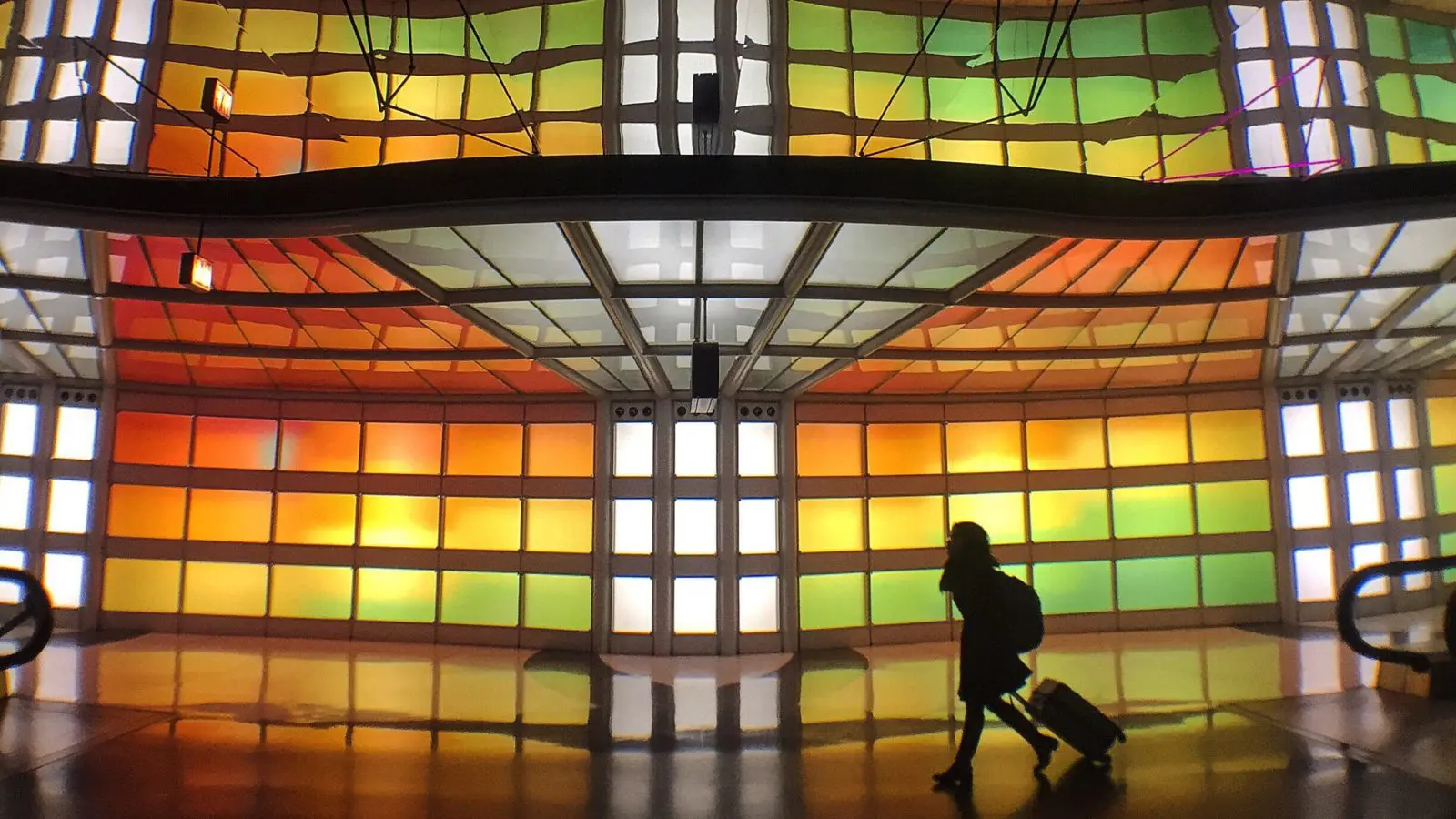 Person rolling luggage in front of stained glass display in airport terminal