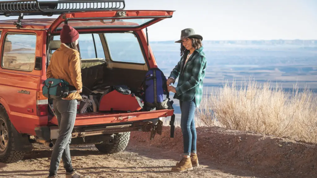 Two people talking near the back of a vehicle with Osprey luggage and backpacks