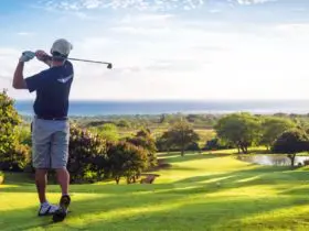 Man hitting golf ball down hill towards ocean and horizon (Photo: Shutterstock)