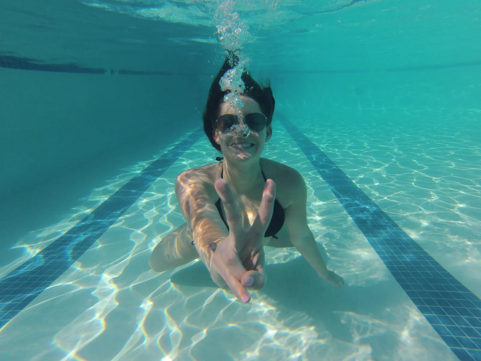 girls getaway in Palm Springs- woman underwater in pool showing peace sign