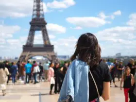 Woman in foreground looking out at a crowd of people walking and standing wearing a wide variety of outfits and shoes with the Eiffel Tower