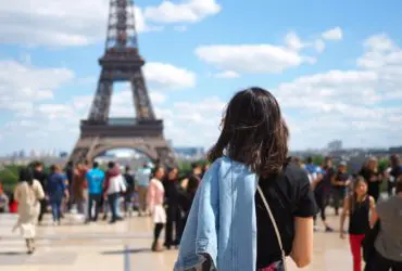 Woman in foreground looking out at a crowd of people walking and standing wearing a wide variety of outfits and shoes with the Eiffel Tower