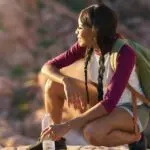 woman wearing travel backpack relaxing on a rock with a waterbottle at sunset