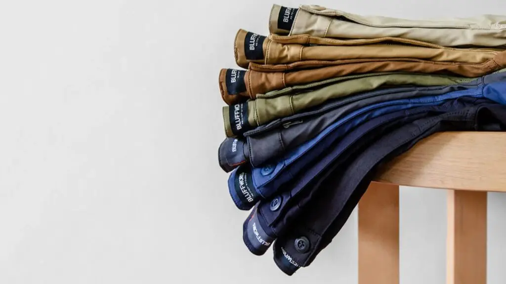 Several pairs of pants draped on a light wood chair