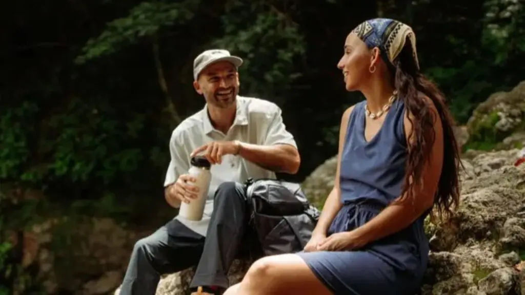 A man holding a water bottle and a woman wearing a head scarf sitting on a rock
