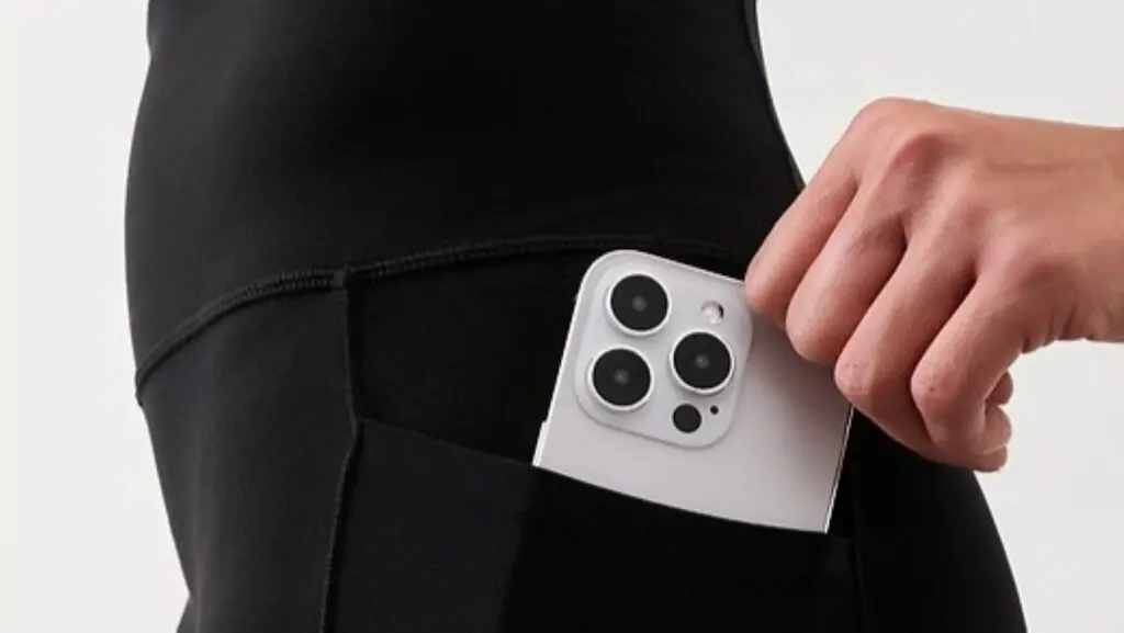 A woman putting a phone into a pocket on a pair of black Athleta leggings