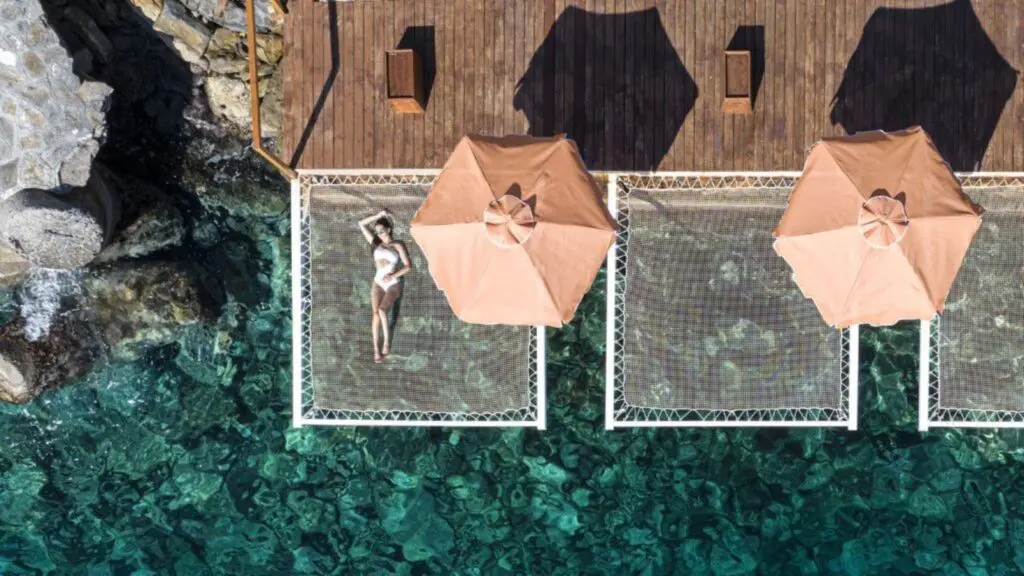 A woman lying on a net lounger over the water at Aquila Elounda Village