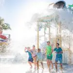 Kids running through the splash pad at Beaches Turks and Caicos waterpark while a giant bucket of water dumps water downward