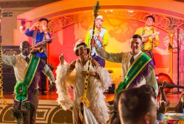 Actors dressed in New Orleans-style costumes singing and dancing on a colorful stage