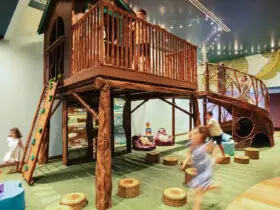 Kids running around a treehouse play structure inside a building