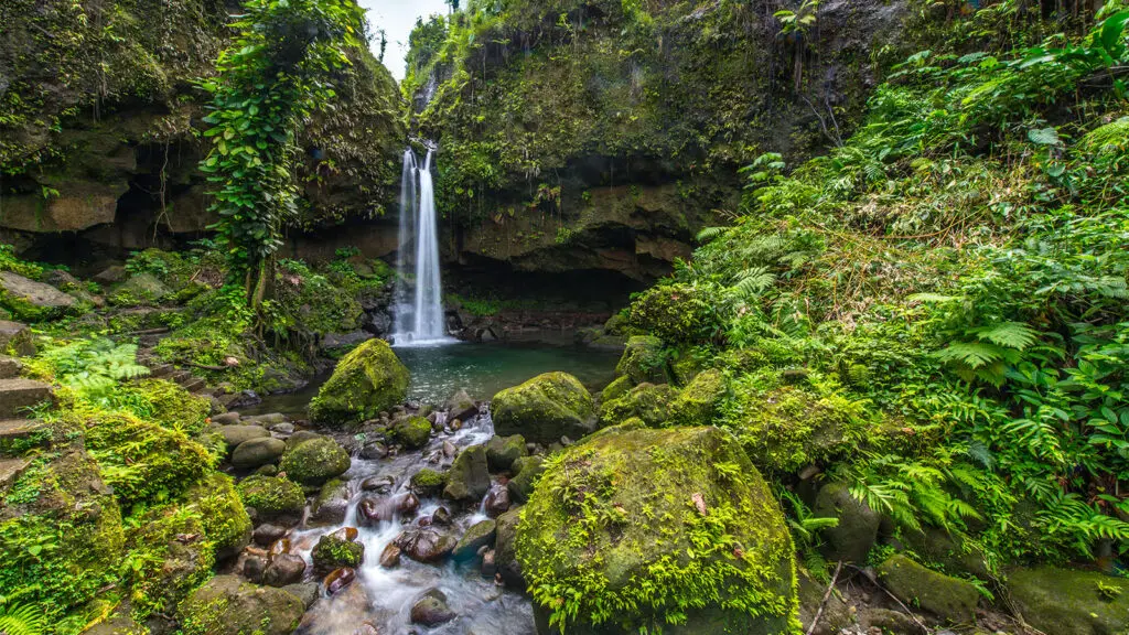 Waterfall spilling into small cove pool surrounded by lush mountains