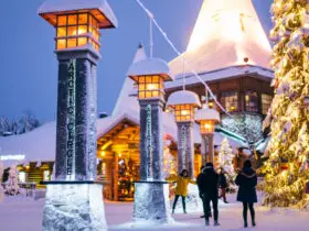 A snowy village surrounded by lanterns, a tall Christmas tree, and people walking around
