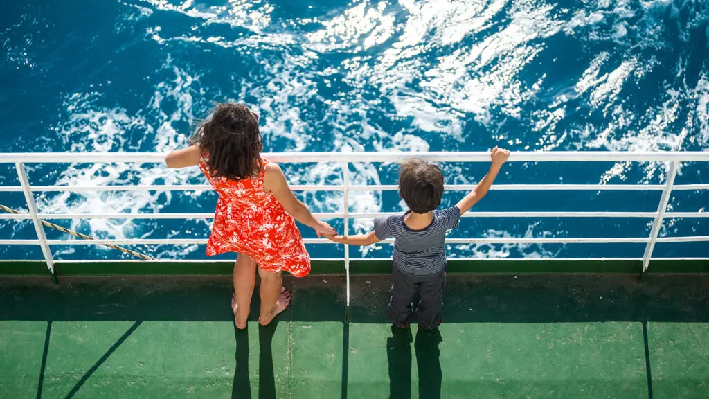 Mother and son holding hands and standing on cruise ship looking into the ocean