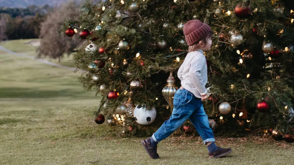 A little kid in a hat running in front of a decorated Christmas tree at Ojai Valley Inn
