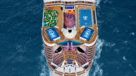 Top deck of cruise ships sailing in ocean, with a sports court, slide, surf simulators, and other features