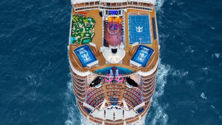 Top deck of cruise ships sailing in ocean, with a sports court, slide, surf simulators, and other features