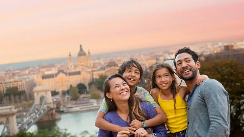 Family hugging each other on top of hill with historic city in the background during sunset