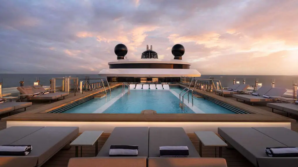 Cruise ship pool surrounded by lounge chairs at sunset