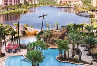 Swimming pool with pirate ship structure next to a lake with buildings in the background