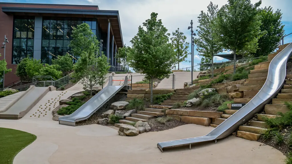 Slides, steps, and rock-climbing walls on hillside next to large glass building
