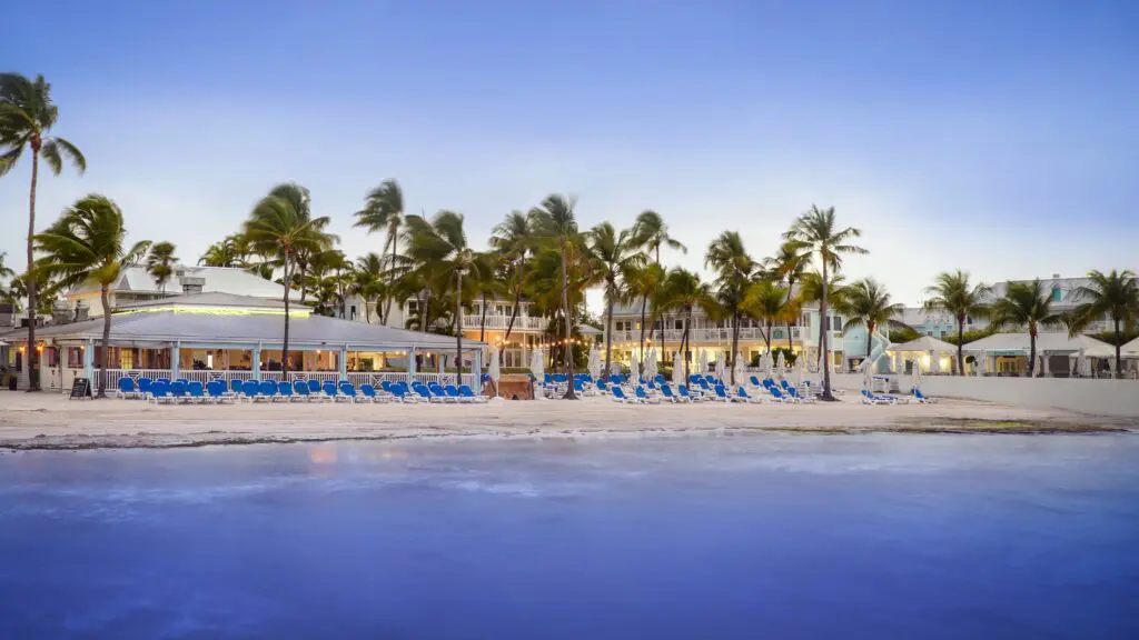 A twilight view of blue lounge chairs on the beach with a restaurant behind them at Southernmost Beach Resort