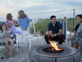 Adults and kids sitting around a firepit on the beach eating s'mores