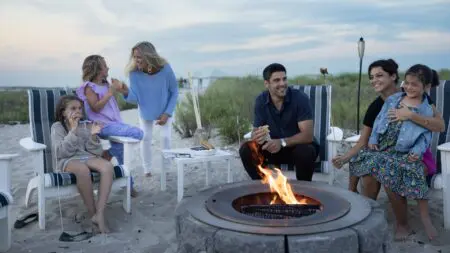 Adults and kids sitting around a firepit on the beach eating s'mores