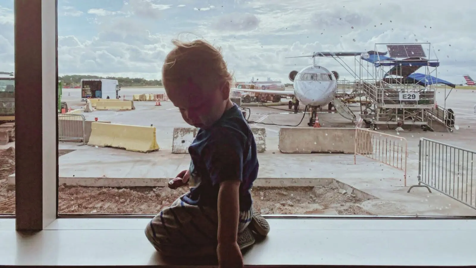toddler sitting at a boarding gate at the airport with a plane in the background
