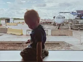 toddler sitting at a boarding gate at the airport with a plane in the background