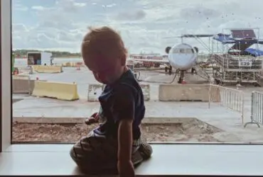 toddler sitting at a boarding gate at the airport with a plane in the background