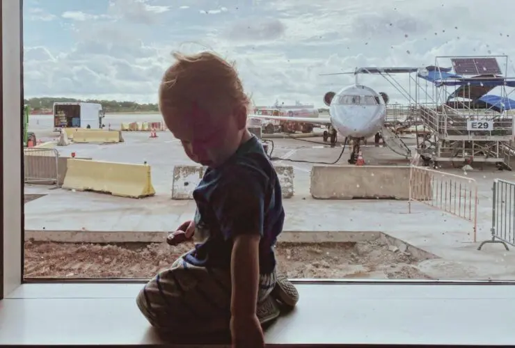 toddler sitting at a boarding gate at the airport with a plane in the background