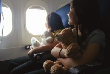 two girls holding stuffed animals sitting on an airplane