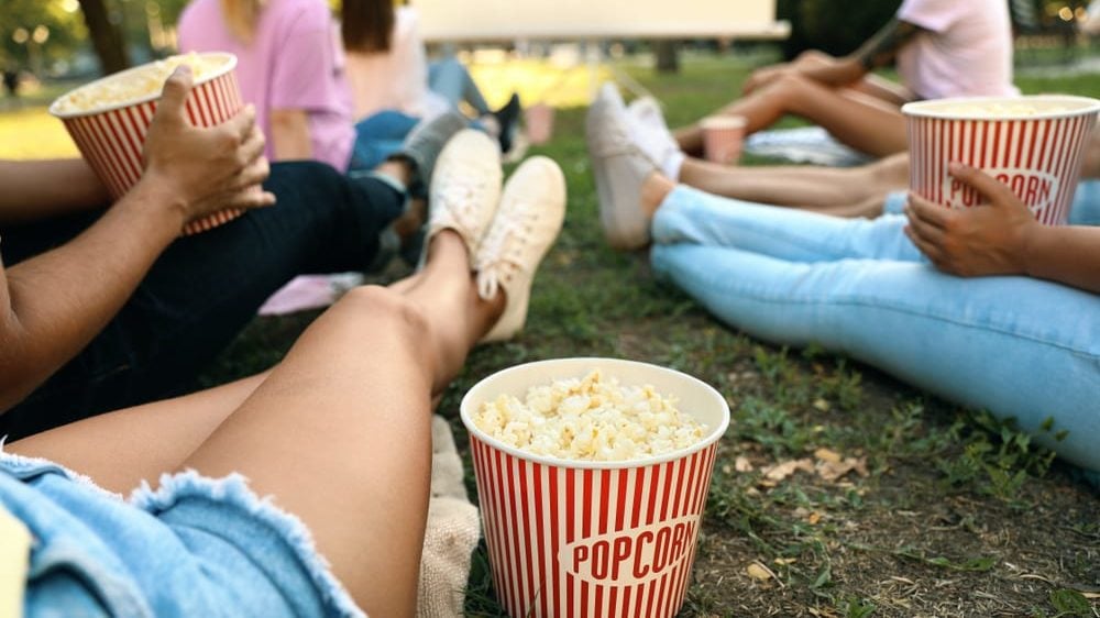Outdoor movie screens: Young people with popcorn watching movie in open air cinema. (Photo: Shutterstock)