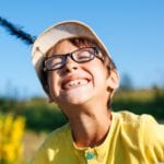 boy wearing glasses and a hat smiling in the sun