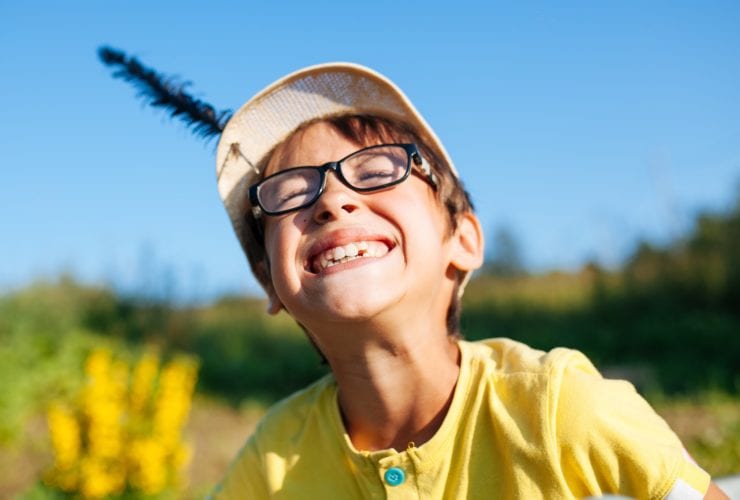 boy wearing glasses and a hat smiling in the sun