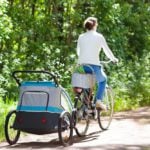 Young mother riding bicycle with baby bike trailer in sunny summer park. (Photo: Shutterstock)