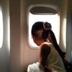 child with ponytail looking out airplane window