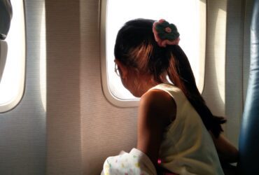 child with ponytail looking out airplane window