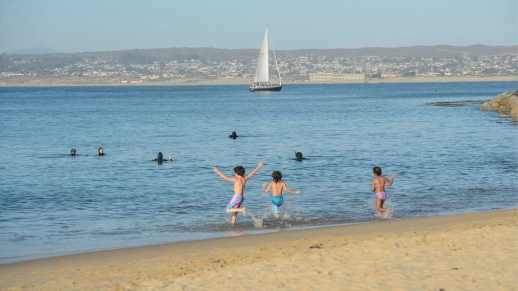 children playing in the water at Monterey State Beach with sailboat in background