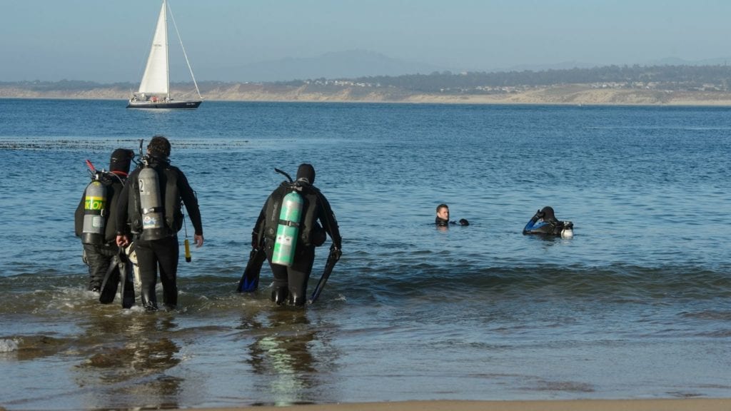 scuba divers going into the water at San Carlos Beach in Monterey